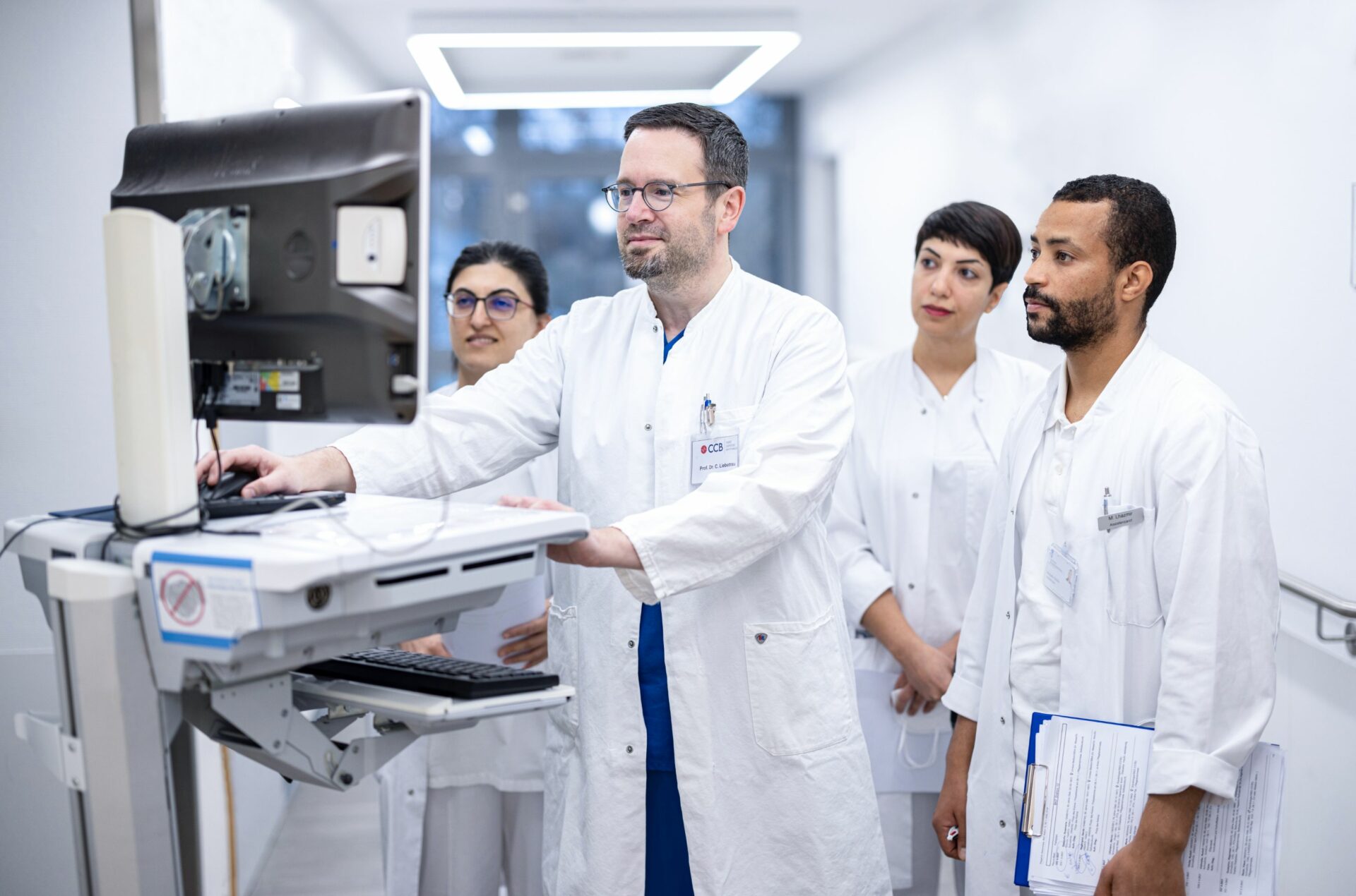 Arzt steht mit seinem Team vor mobiler Arbeitsstation mit Monitor