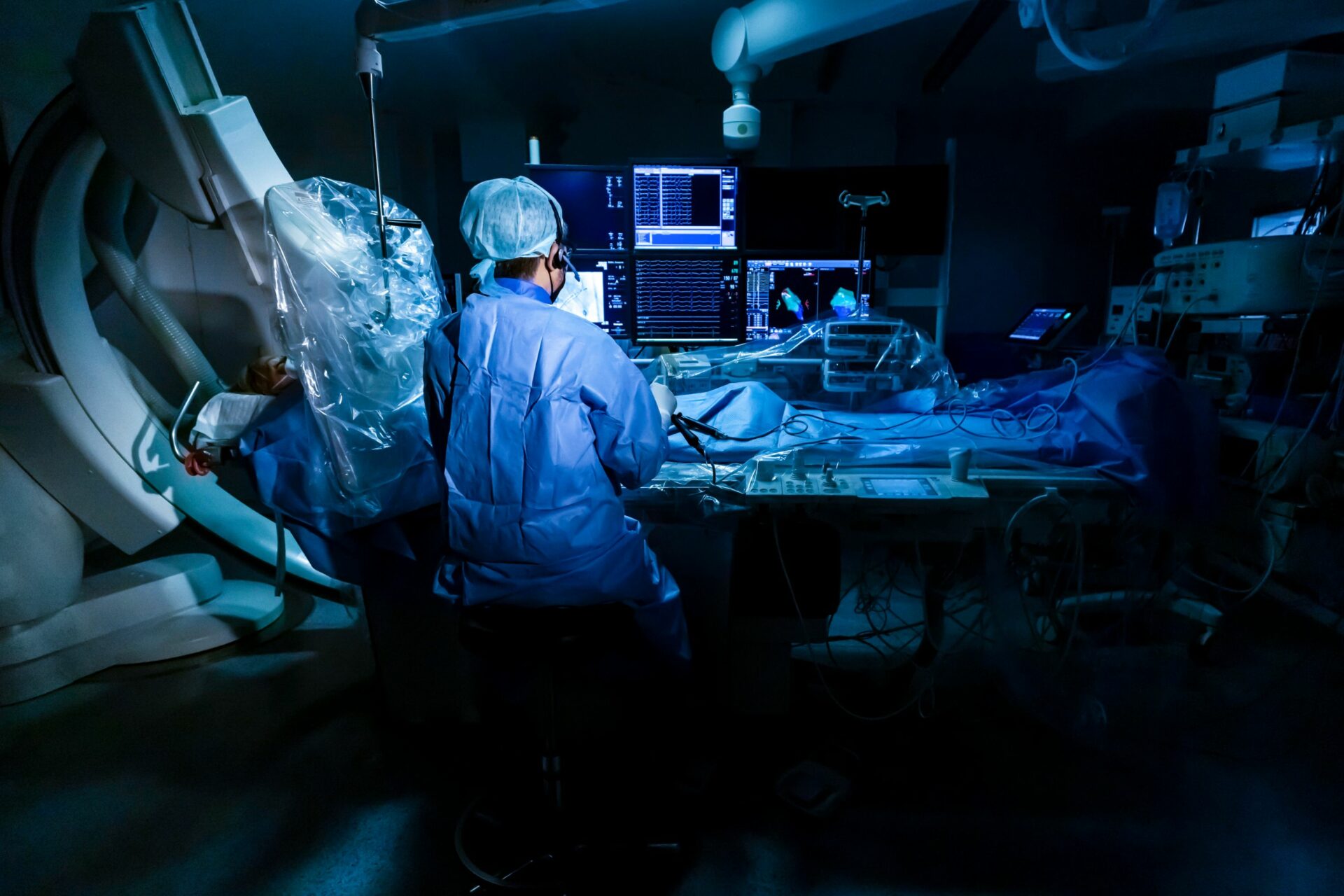 Arzt sitzt im abgedunkelten OP-Raum und führt eine Ablation an einem vor ihm liegenden Menschen durch